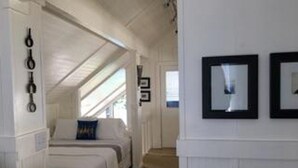 Un cuarto de hotel con un largo pasillo que conduce a una zona con cama, una ventana con persianas y cuadros en la pared.