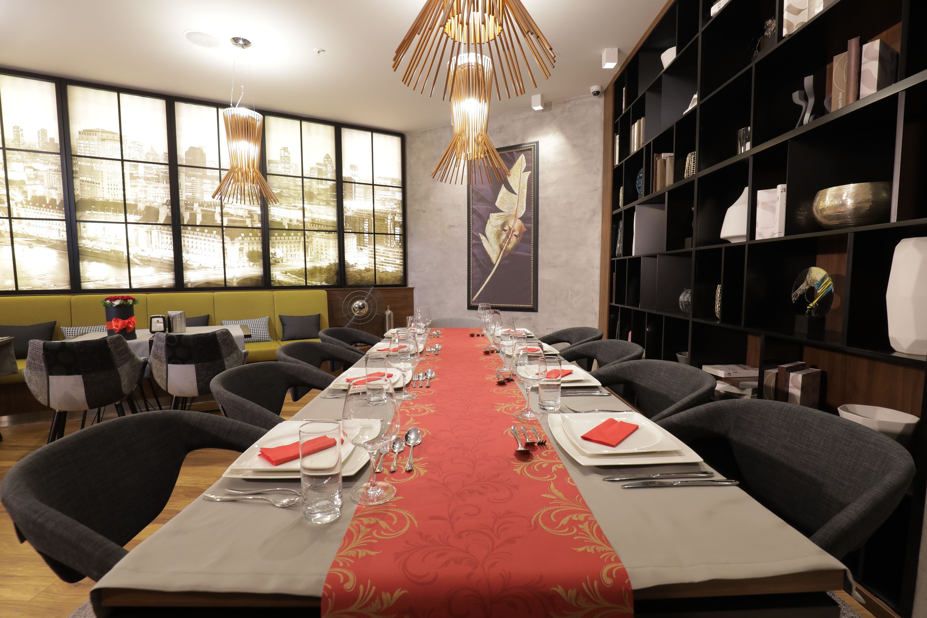 Una sala menjador amb una taula llarga preparada per a dinar, caires, una paret decorativa i una prestatgeria.