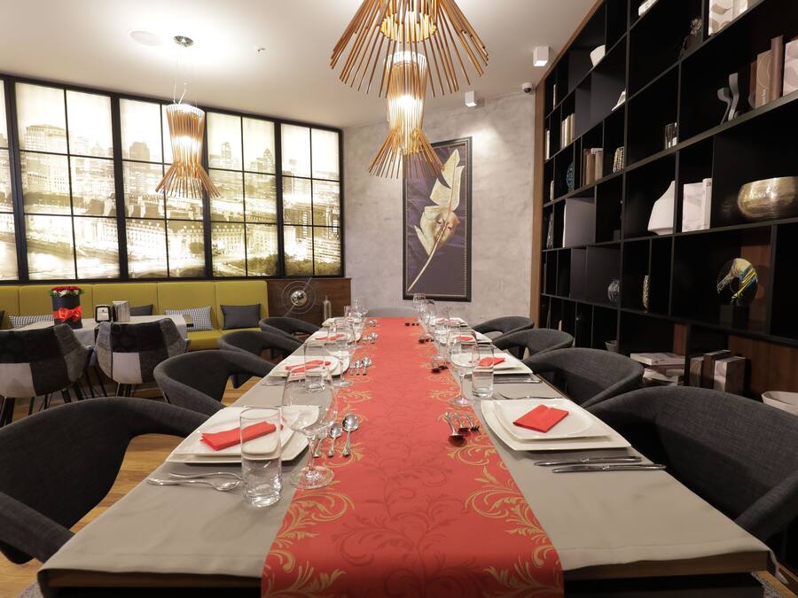 Una sala menjador amb una taula llarga preparada per a dinar, caires, una paret decorativa i una prestatgeria.