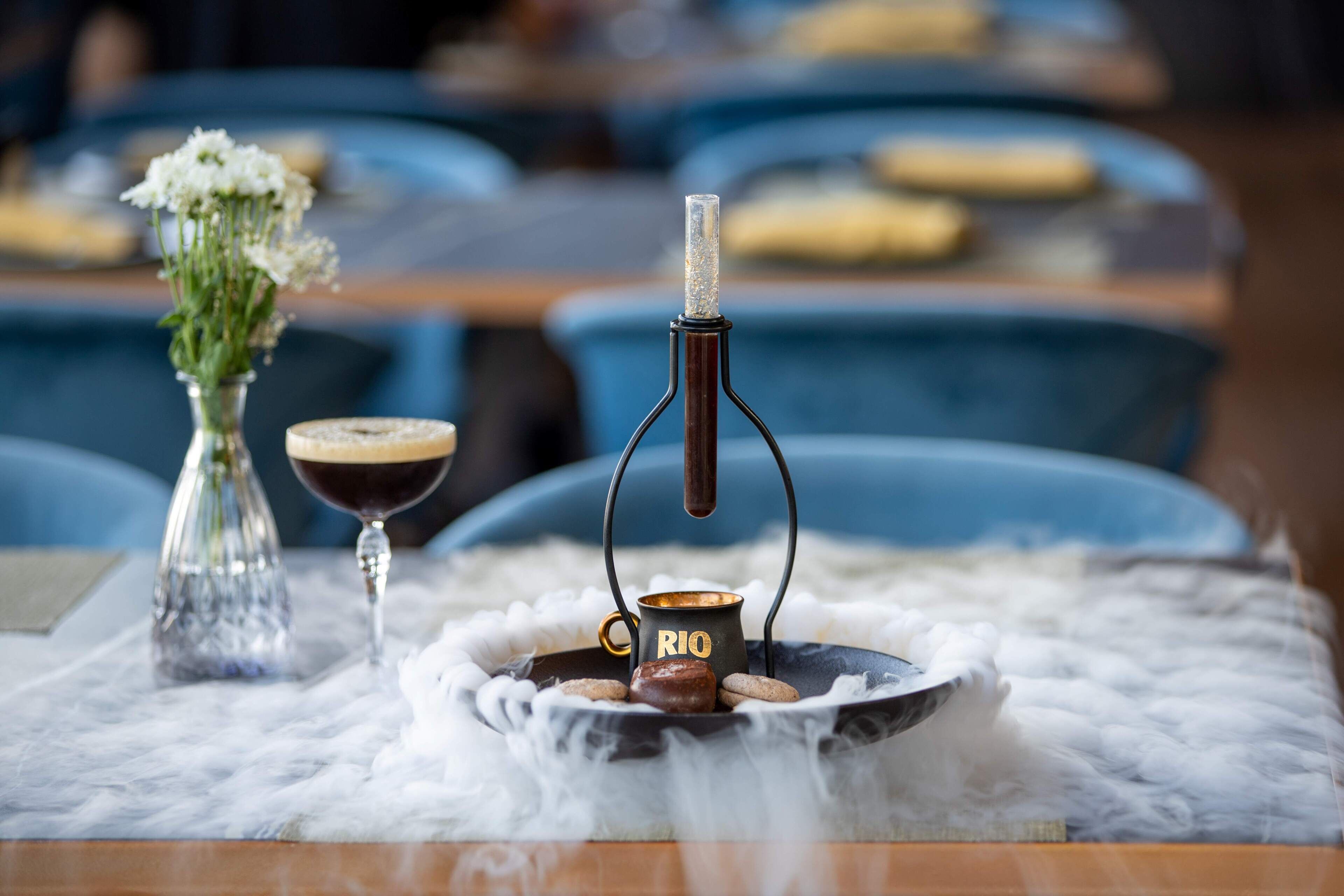Een tafel met een waterpijp, een glas wijn en een kleine vaas met bloemen.