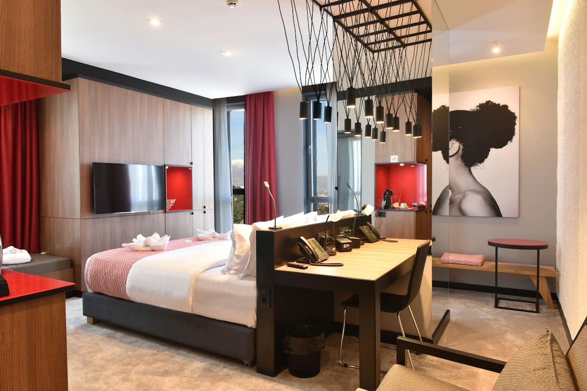 Una habitación de hotel moderna con una cama grande, un escritorio, un televisor y un cuadro en la pared.
