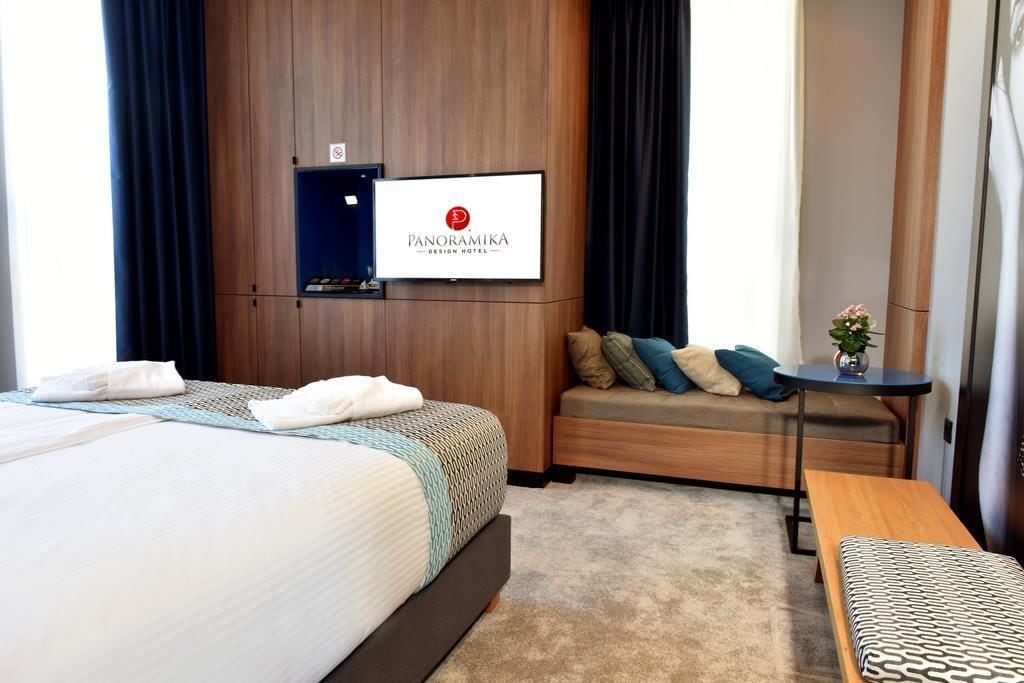 A hotel room with a bed, a sofa, a small table, and a TV mounted on the wall.