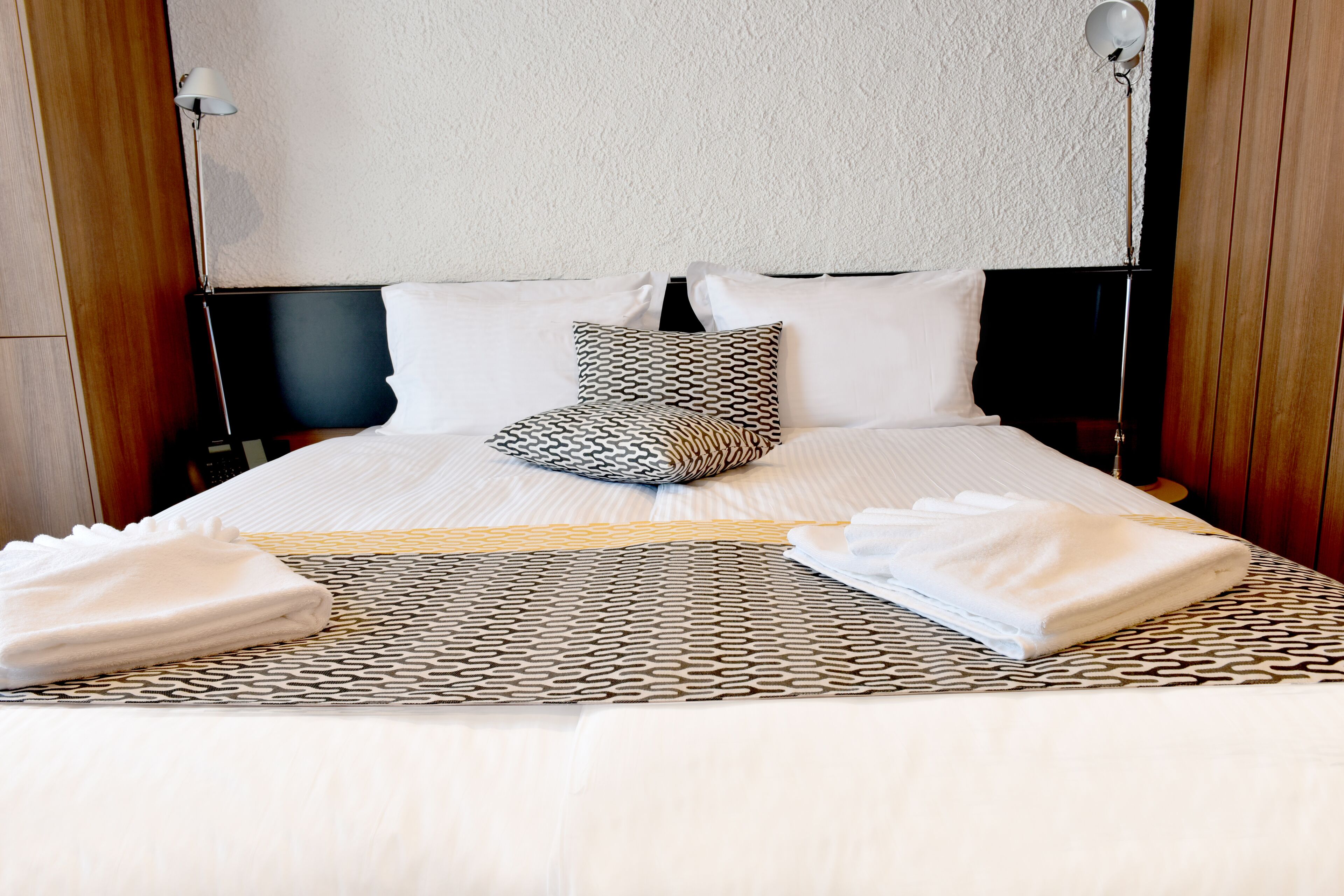 Una cama bien tendida con ropa de cama estampada, una almohada y dos toallas dobladas.