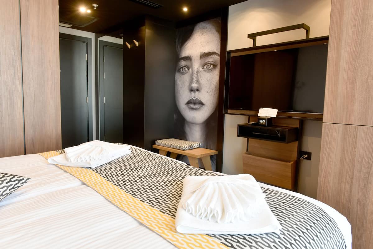 Habitación de hotel con una cama grande, una mesita de noche, un espejo y un cuadro colgado en la pared.