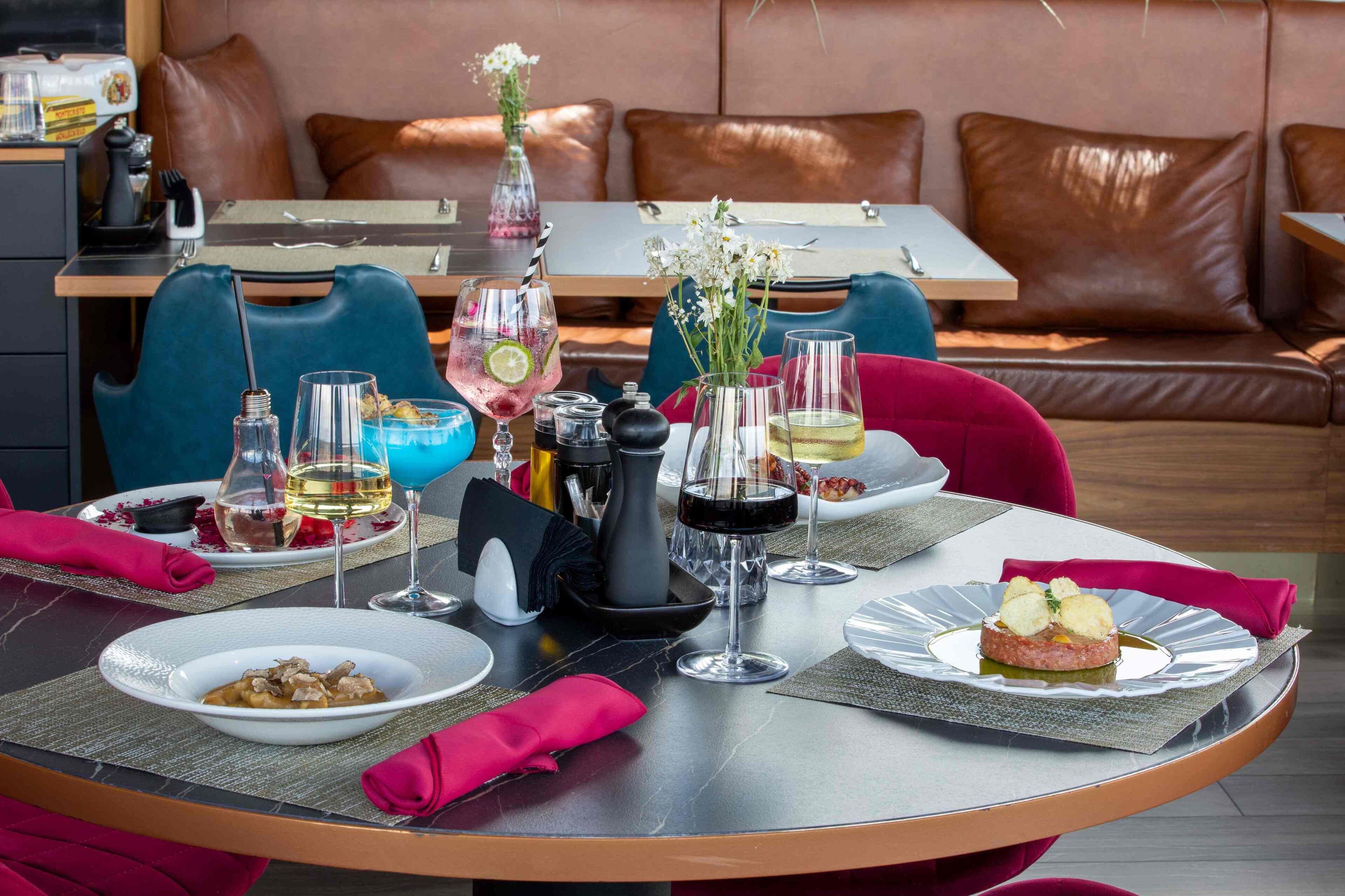 Una mesa de comedor dispuesta con platos de comida, copas de vino y un florero con flores.