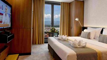 Quarto de hotel com cama, televisão, escrivaninha e vista para a cidade.