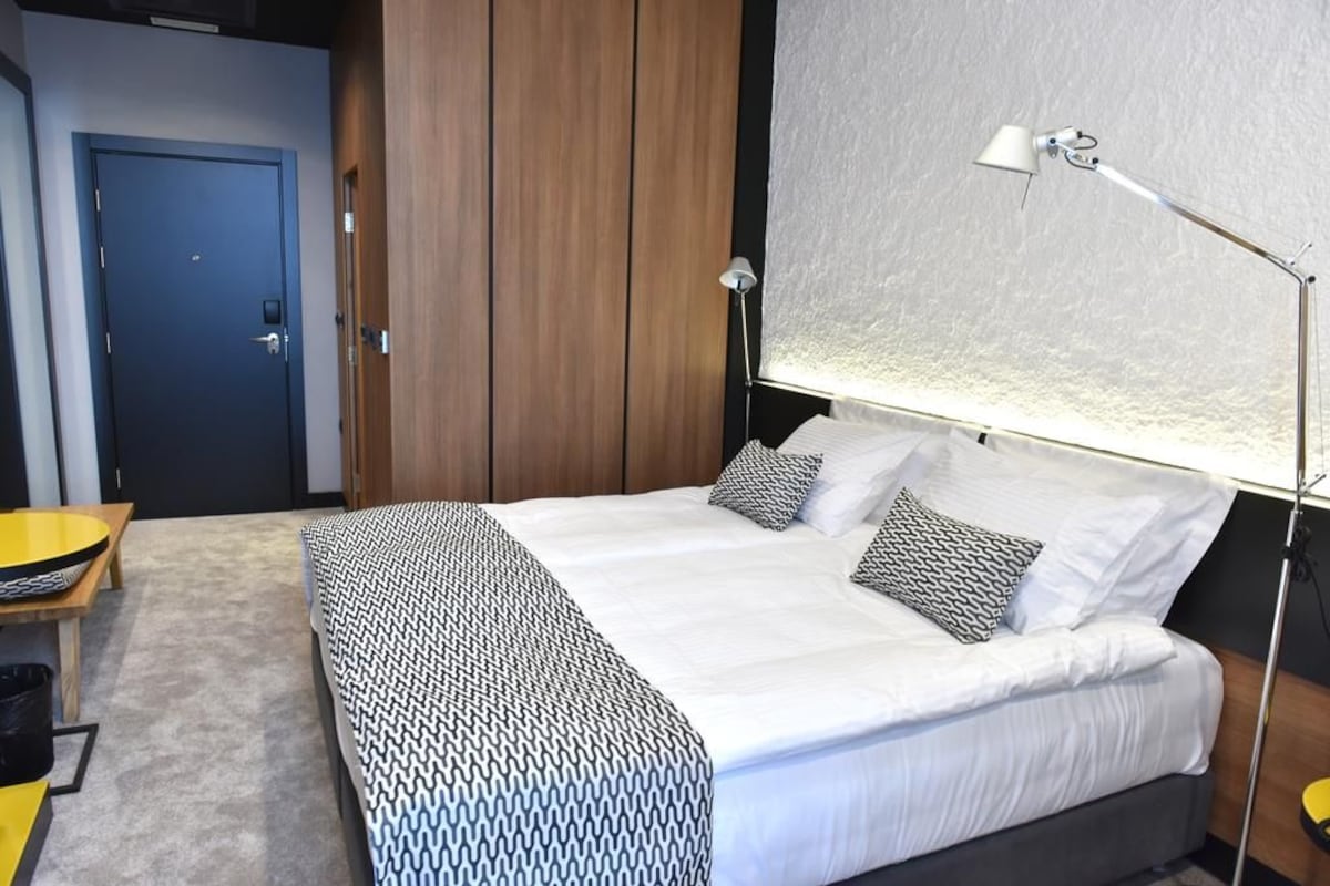 A bedroom with a bed, bedside lamp, and a view of the outside.