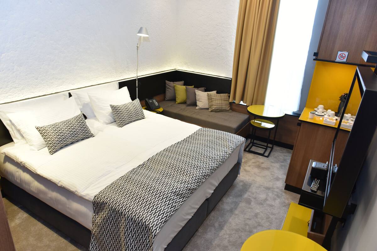 Una habitación de hotel con una cama grande, un escritorio, una silla y una mesita de noche con artículos de aseo.