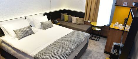 A hotel room with a large bed, a desk, a chair, and a small table with toiletries.