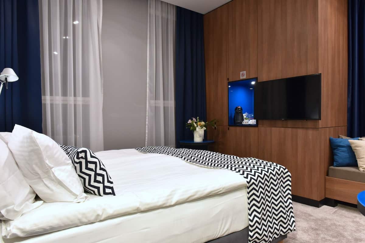 Una habitación de hotel moderna con una cama grande, un televisor de pantalla plana montado en la pared y una mesita de noche con un florero.