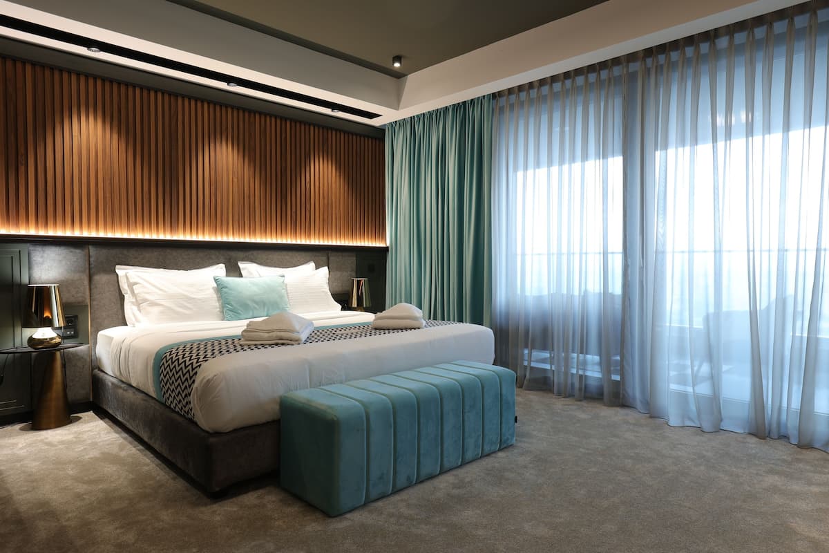 Un dormitorio moderno con una cama grande, un banco y una mesita de noche con lámpara.