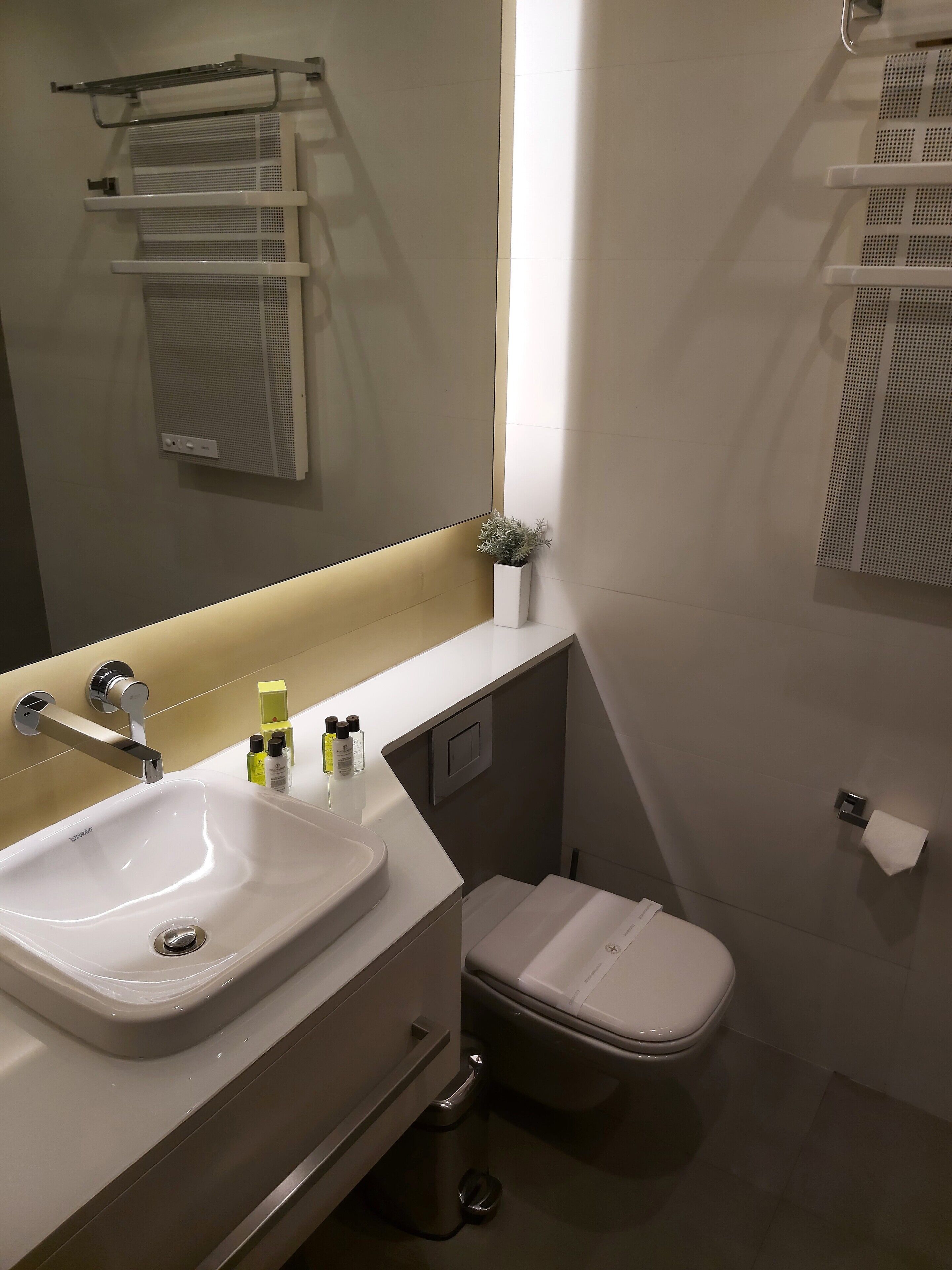 A modern bathroom with a white sink, a toilet, and a small trash bin.