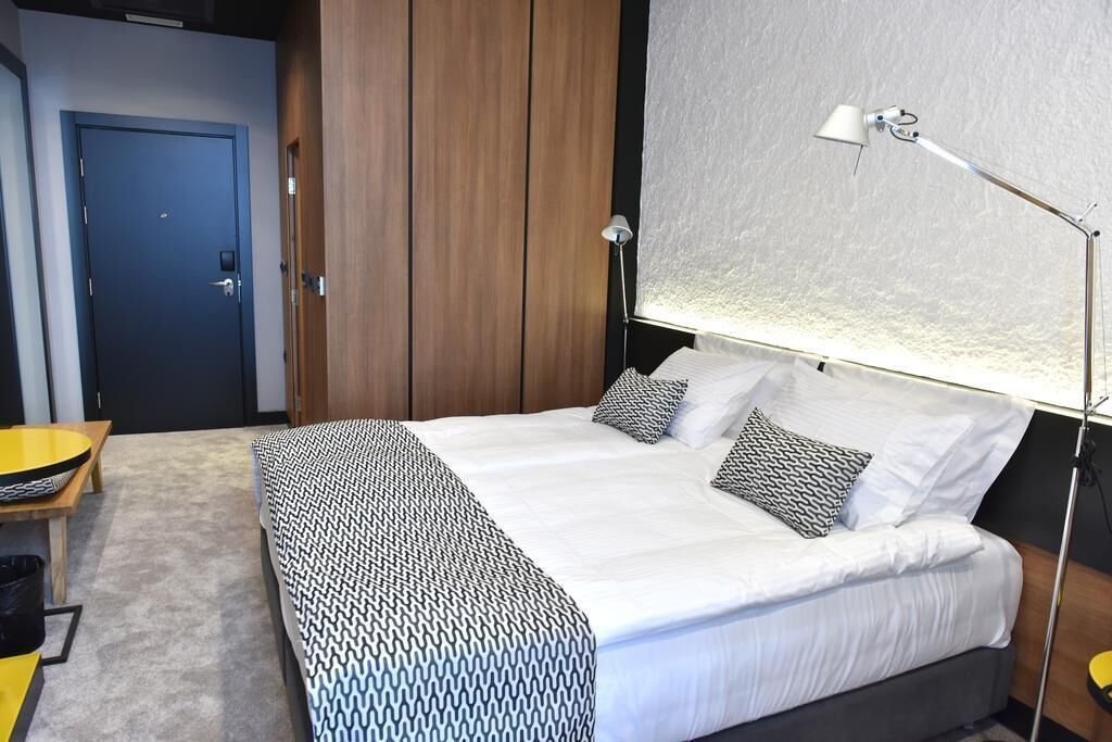 A bedroom with a bed, bedside lamp, and a view of the outside.