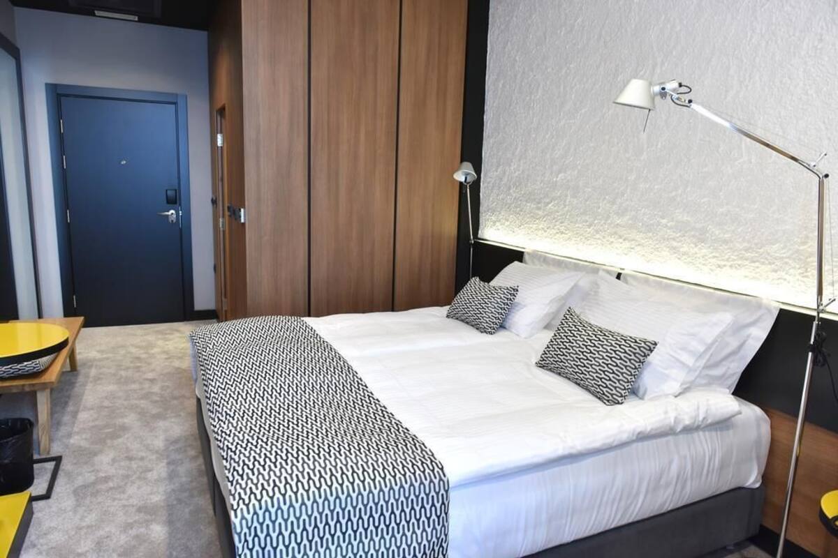 Un dormitorio con cama, lámpara de noche y vistas al exterior.