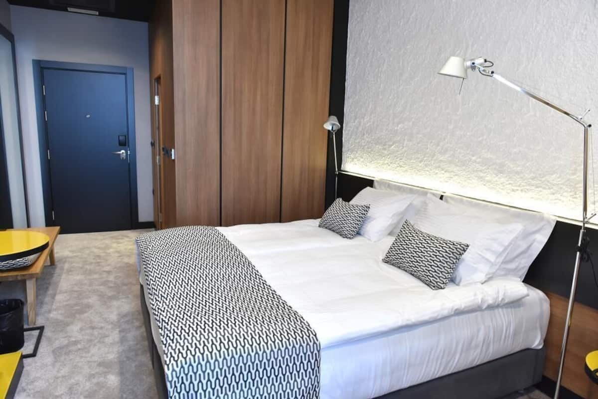 A bedroom with a bed, bedside lamp, and a view of the outside.