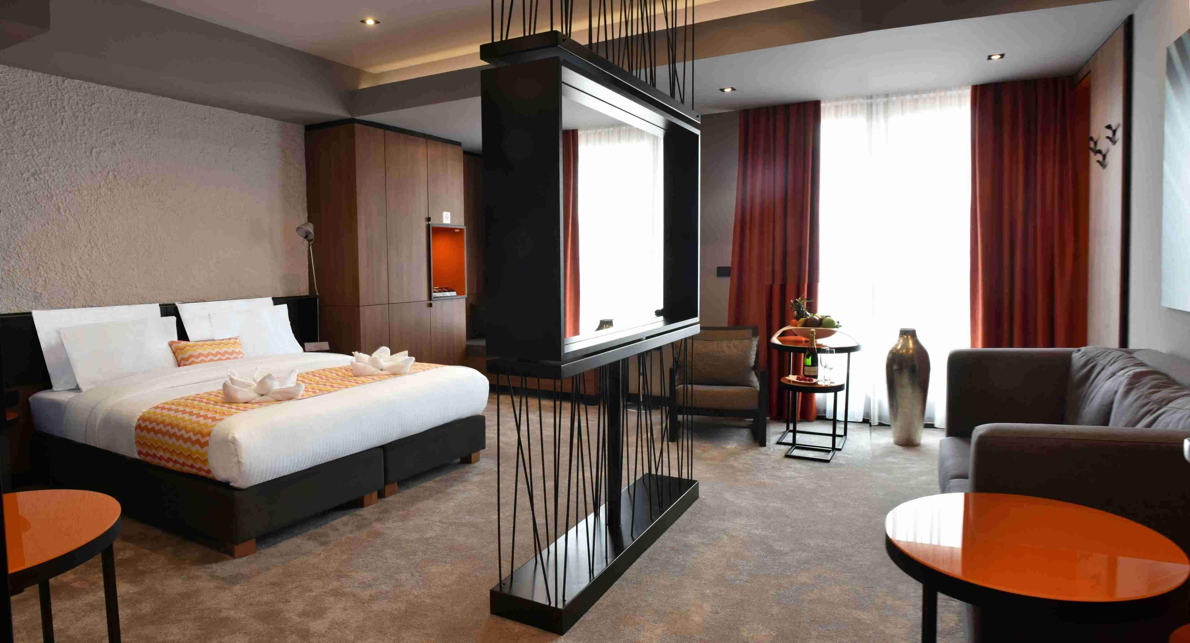 Una habitación de hotel con una cama, televisión, sofá, mesa de centro y una mesita de noche con lámpara.