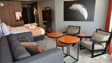 Una habitación de hotel moderna con una cama grande, un sofá, dos mesitas redondas y una silla.