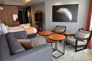 Una habitación de hotel moderna con una cama grande, un sofá, dos mesitas redondas y una silla.