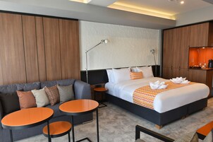 Una habitación de hotel moderna con una cama grande, un sofá, dos mesitas pequeñas y un televisor montado en la pared.