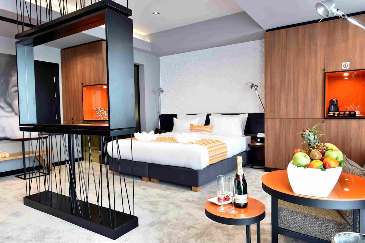 Una habitación de hotel moderna con una cama, una mesita con un frutero, una botella de champán y una mesita de noche.