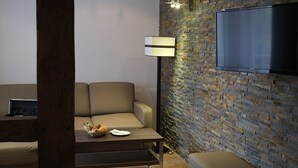 Una sala de estar moderna con una pared de ladrillo, un televisor de pantalla plana, un sofá, una mesa de centro con fruta y una lámpara de pie.