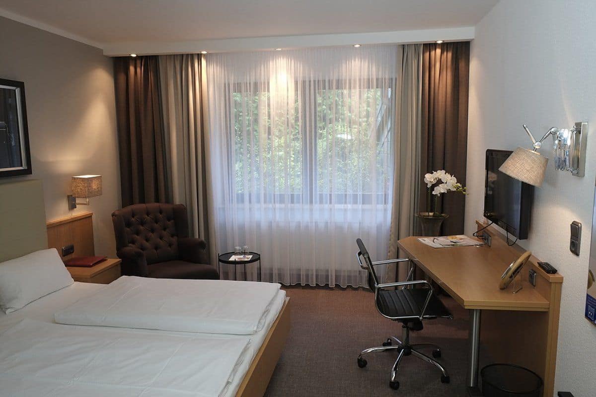 A hotel room with a bed, a desk, a chair, a small table, and a TV.