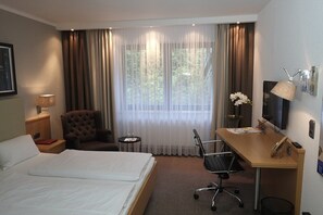A hotel room with a bed, a desk, a chair, a small table, and a TV. - Hotel Brunnenhof International (Wedemark)