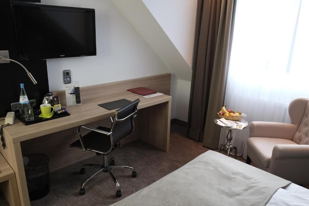 A hotel room with a desk, chair, bed, TV, and a small table with fruit.