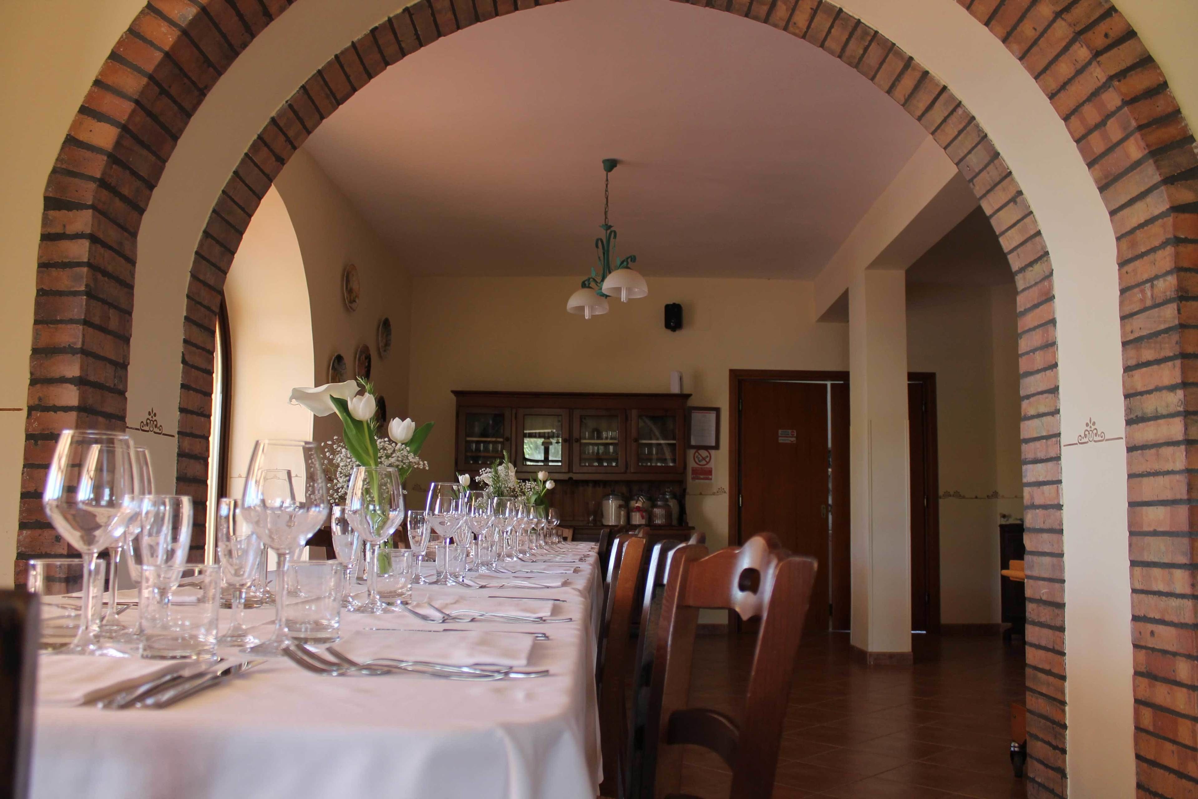 Un comedor con una larga mesa preparada para una comida, arcos de ladrillo y una lámpara colgante.
