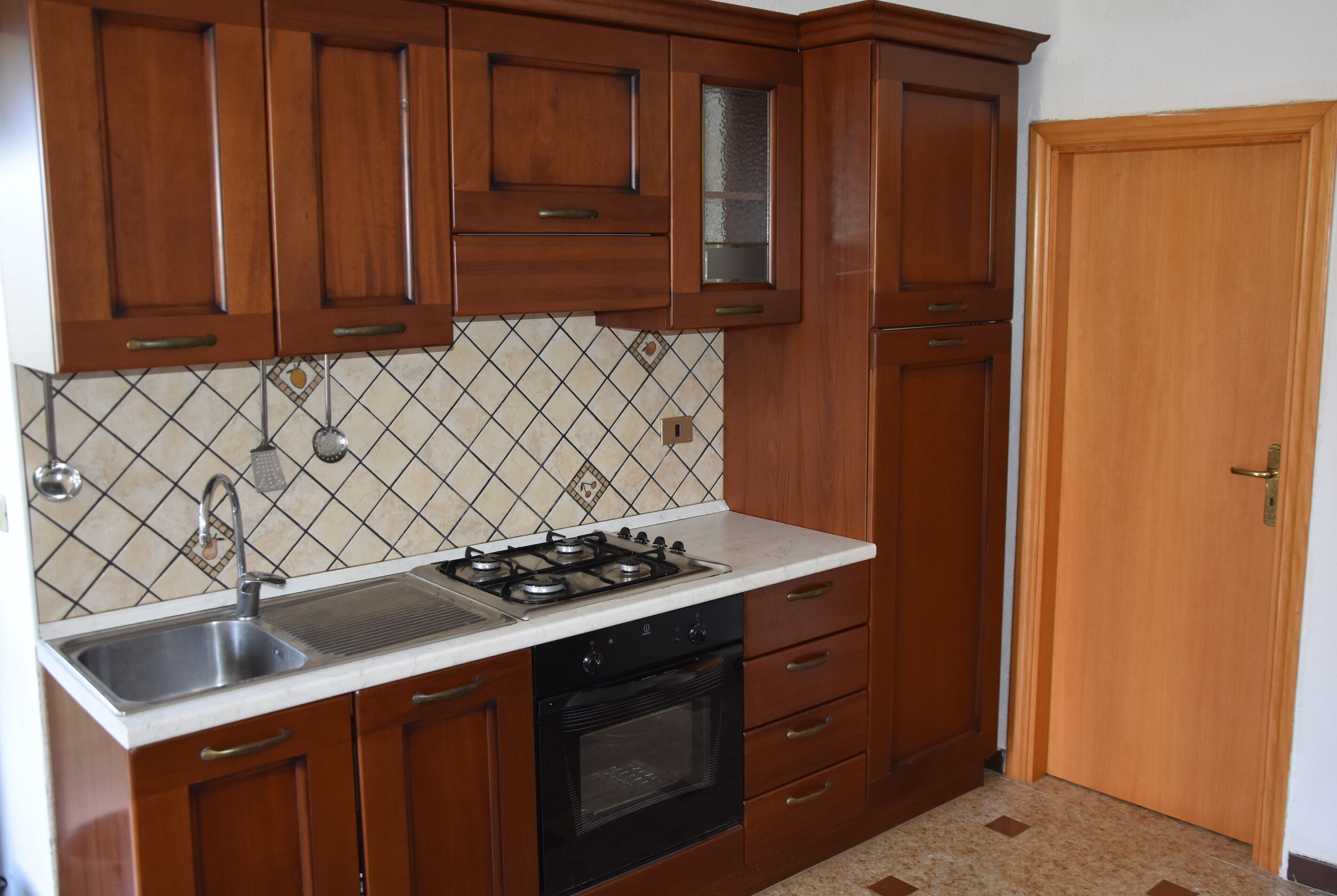 Una cocina con armarios de madera, un lavamanos de acero inoxidable, una estufa a gas y un salpicadero de azulejos.