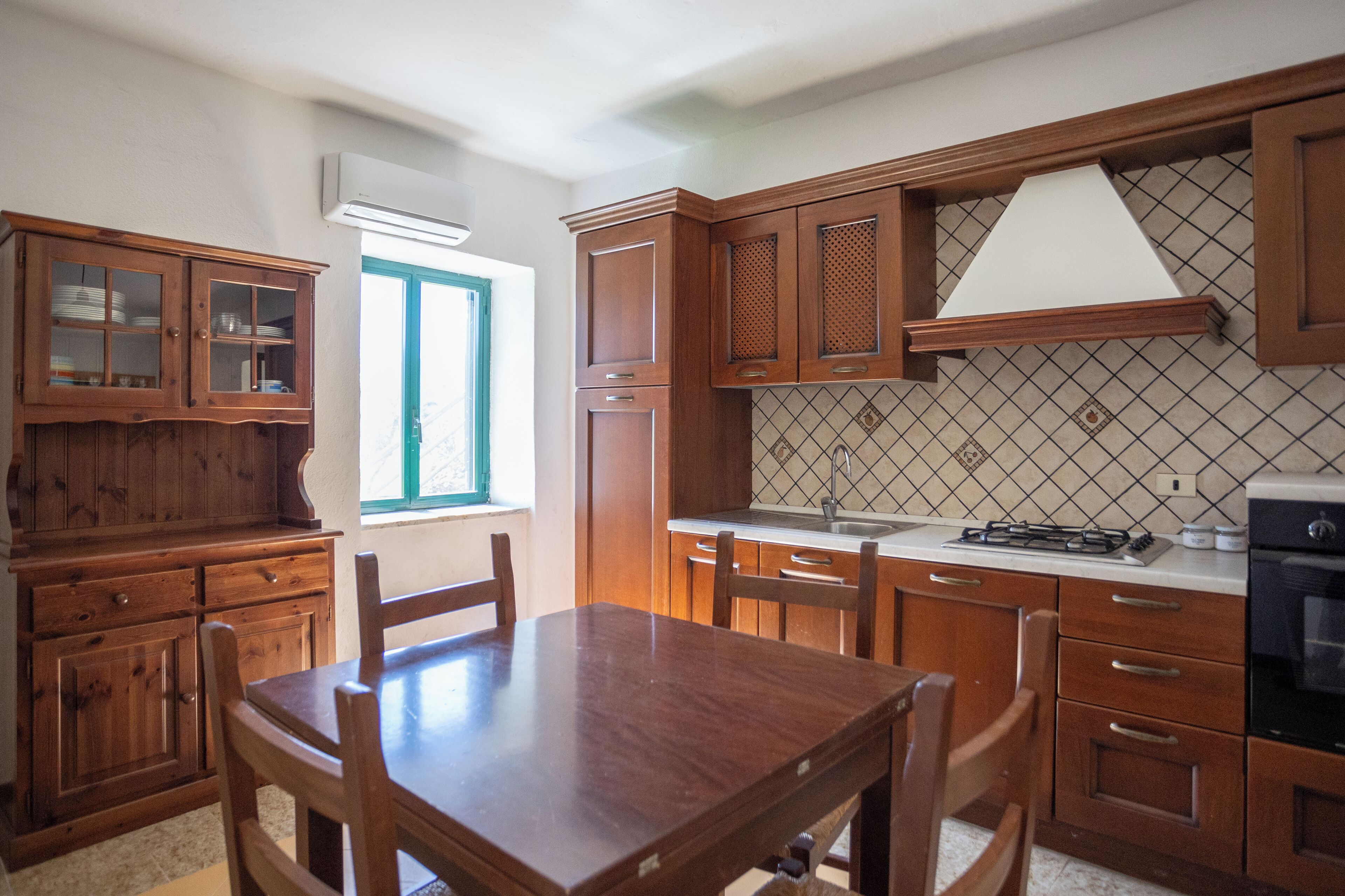A kitchen with wooden cabinets, a dining table, chairs, and a stove.