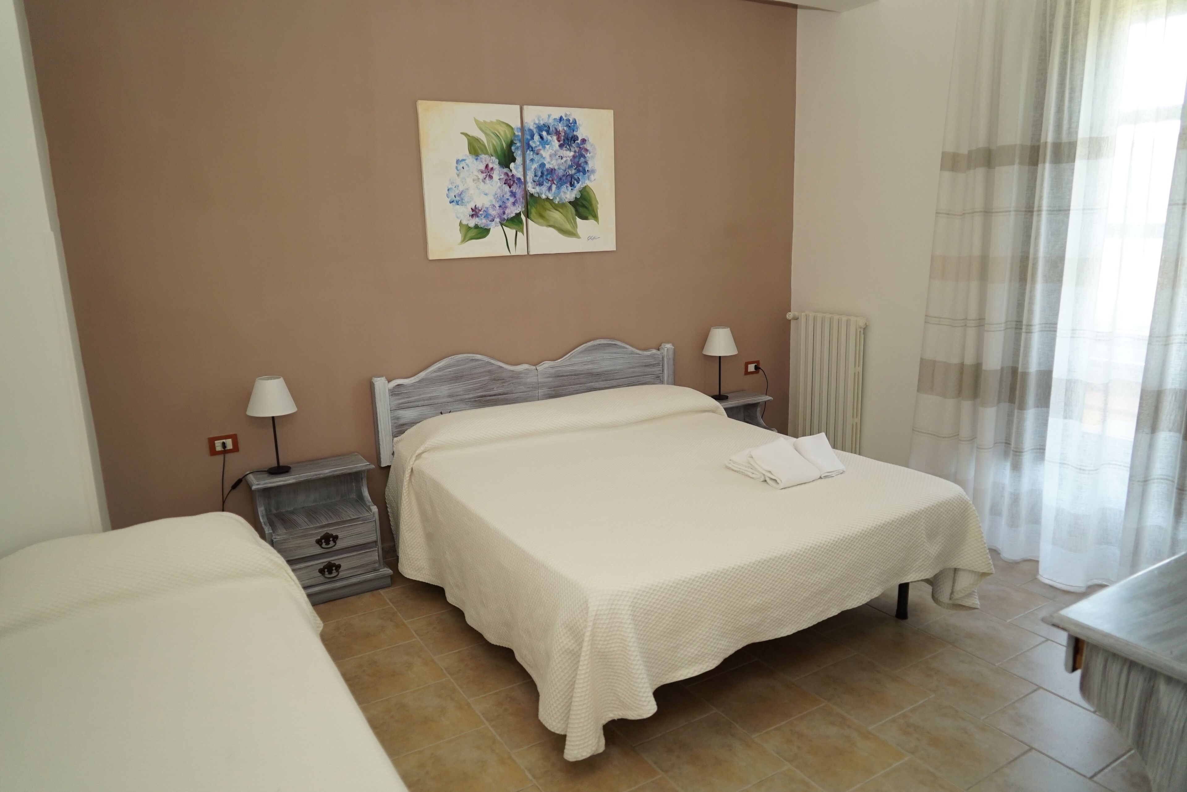 A bedroom with a bed, bedside tables, a lamp, a radiator, and a painting on the wall.