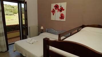 A bedroom with two beds, a view of a garden through an open door, a painting of red flowers on the wall, and a bedside lamp.