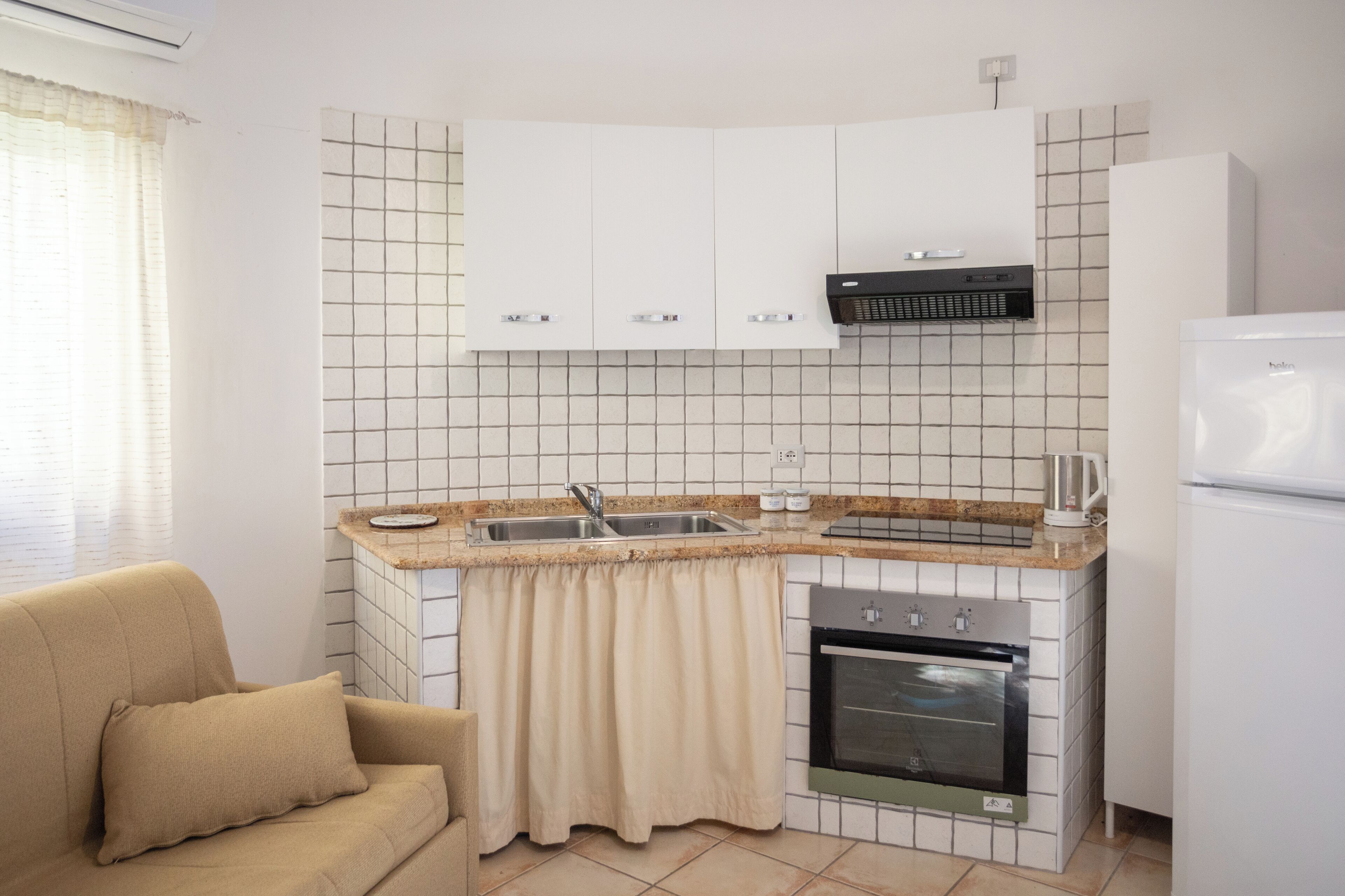 Cuina petita amb armaris blancs, forn integrat, rentapelats i cafetera.