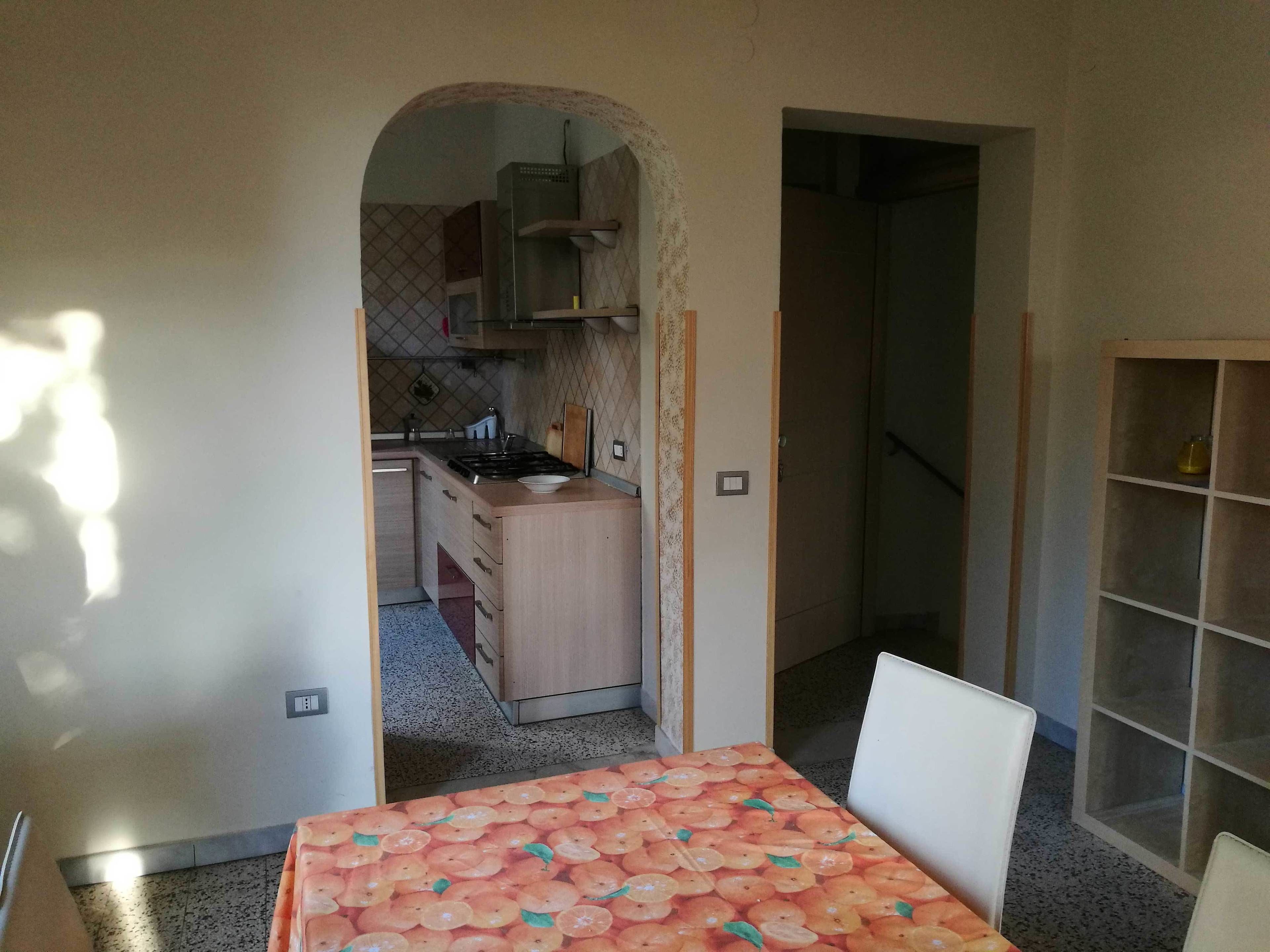 Una cocina con estufa, lavamanos y armarios, que da paso a un comedor con mesa y sillas.