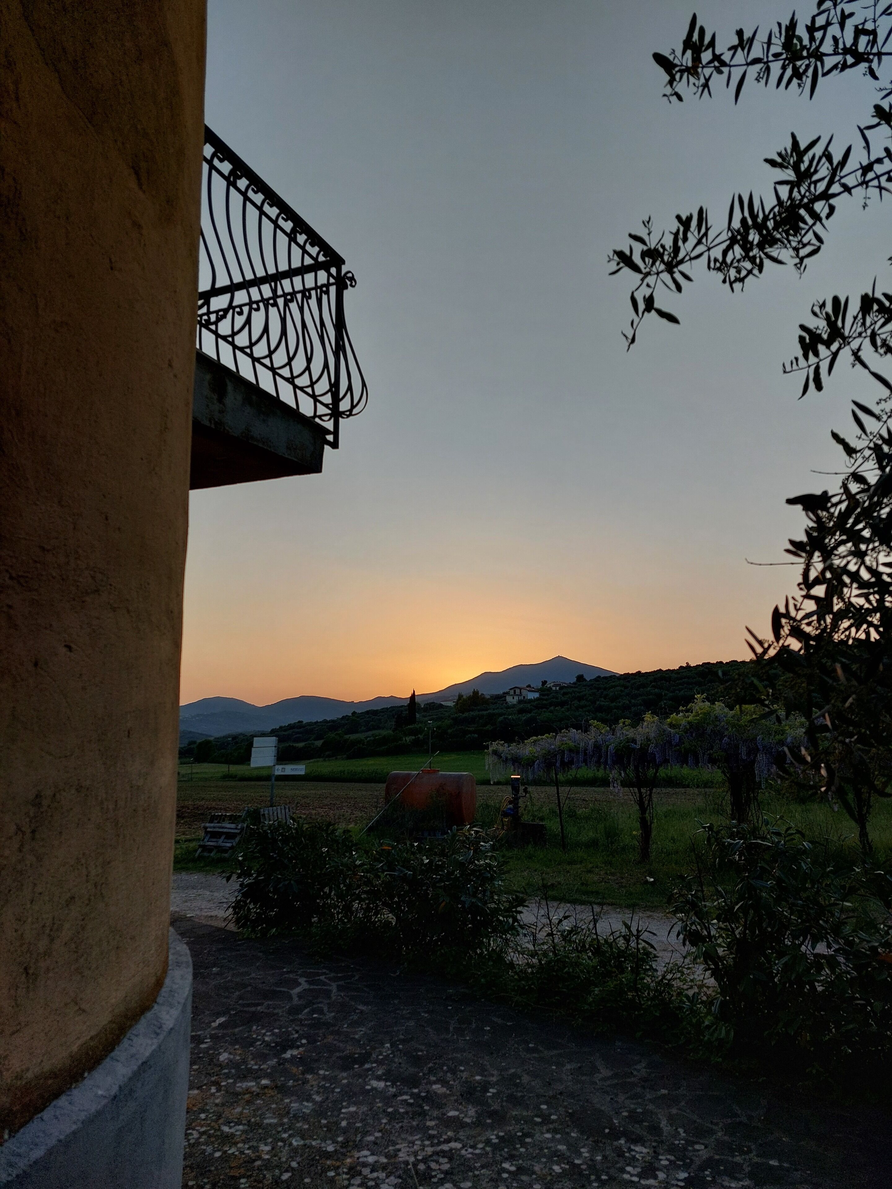 Vista de un paisaje rural con un atardecer, campos y montañas al fondo.