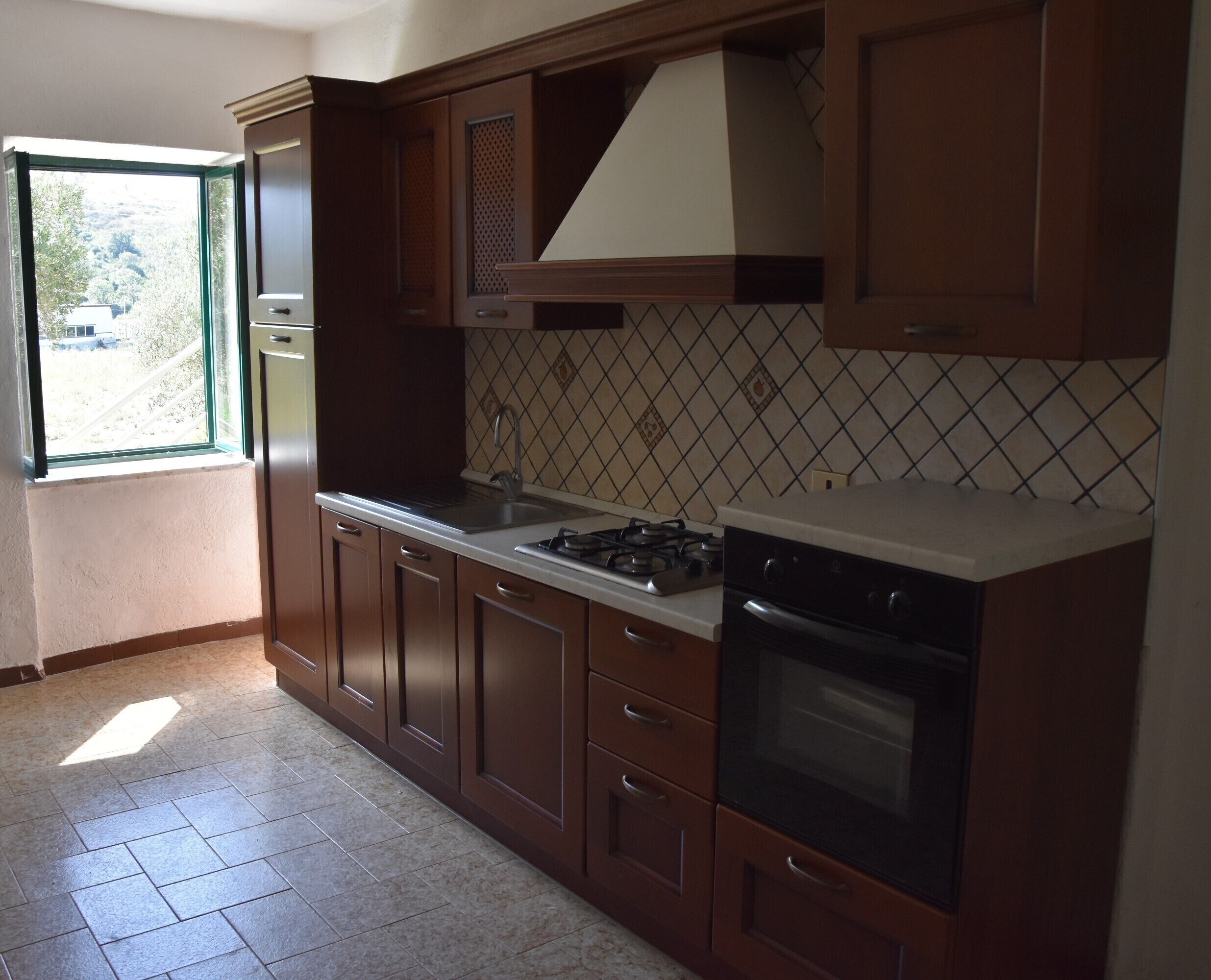 A kitchen with wooden cabinets, a gas stove, a sink, and a window with a view of greenery.