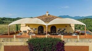 A building with two large umbrellas providing shade over outdoor seating, a tiled roof, and a view of distant mountains. - Agriturismo La Petrosa (Ceraso)