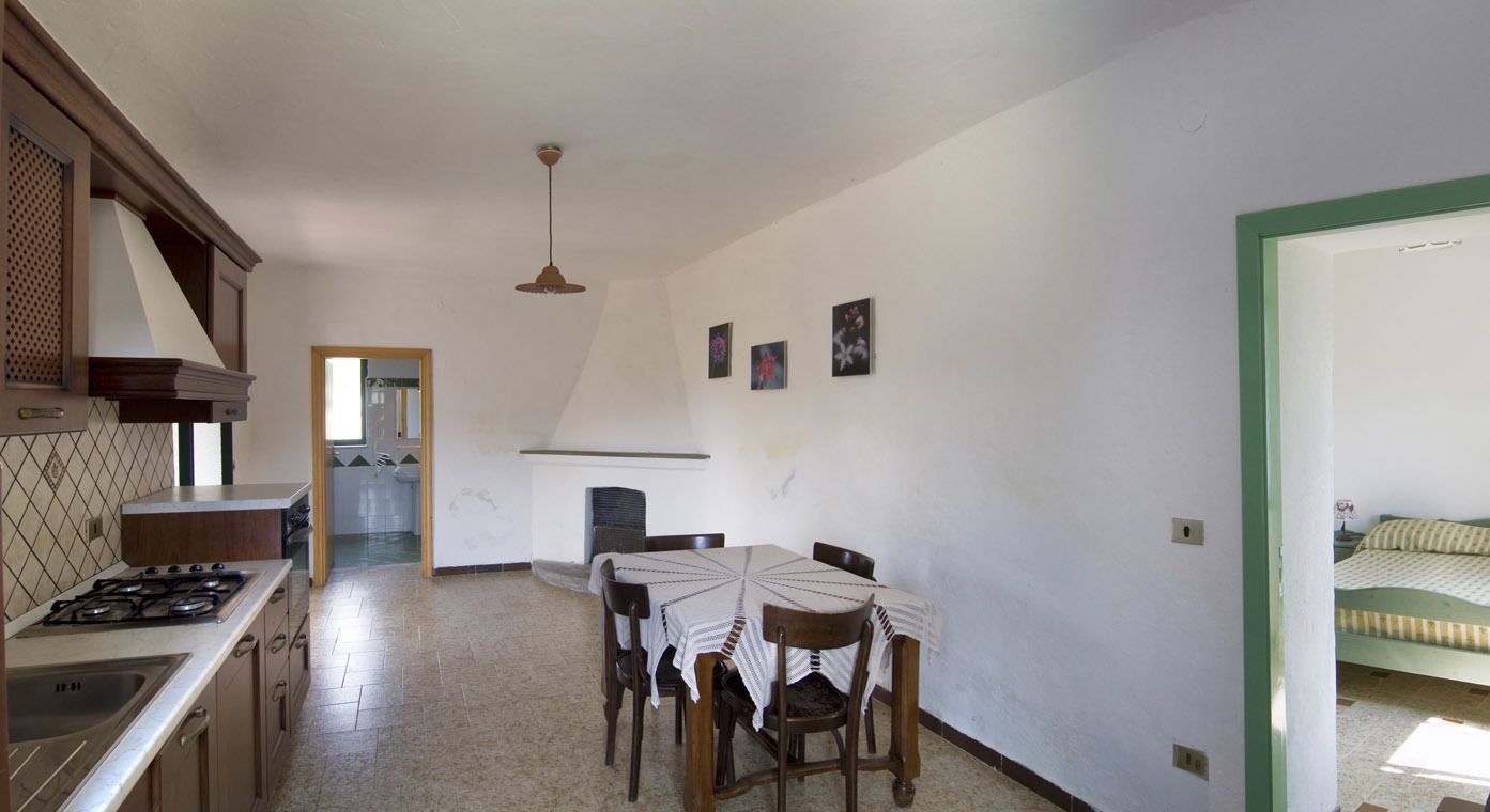 Una cocina con estufa, pileta y mesa de comedor con sillas. Hay una chimenea y una cama en la habitación contigua.