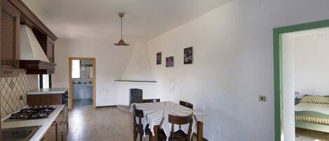 Una cocina con estufa, pileta y mesa de comedor con sillas. Hay una chimenea y una cama en la habitación contigua.