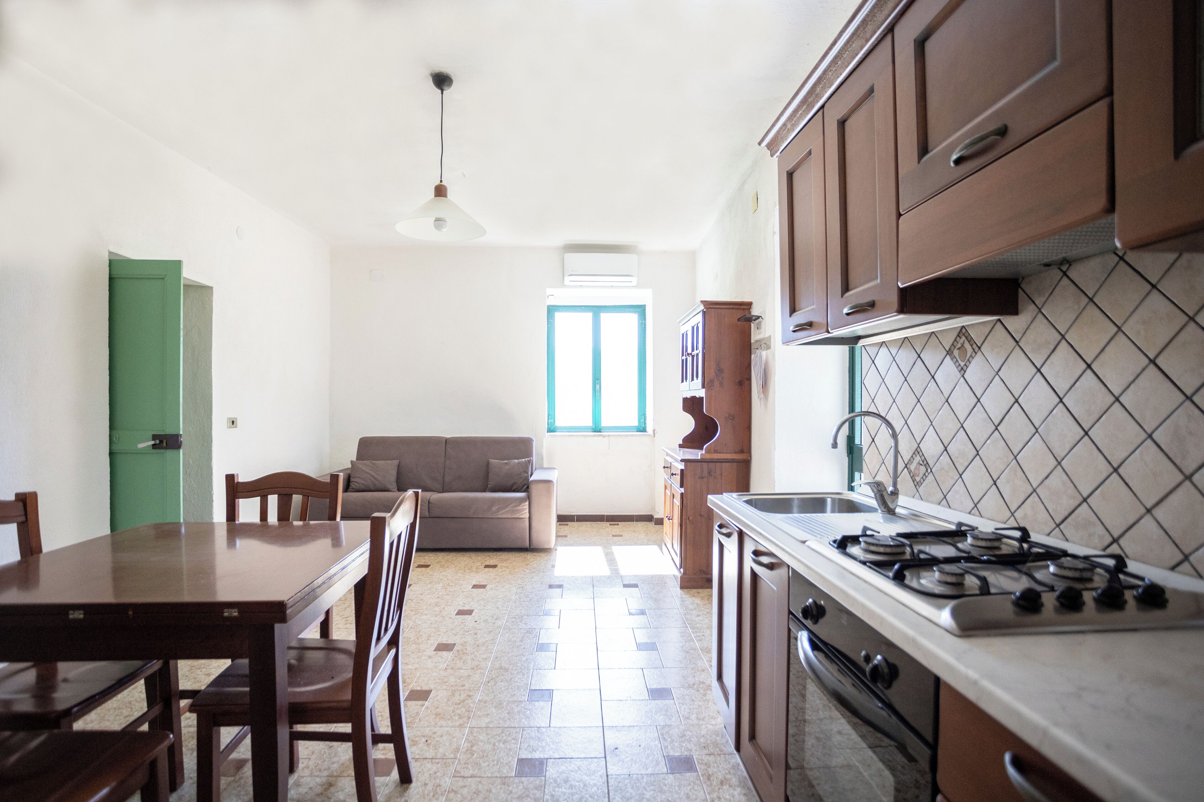 A compact kitchen with a dining table, chairs, a sofa, and a window providing natural light.