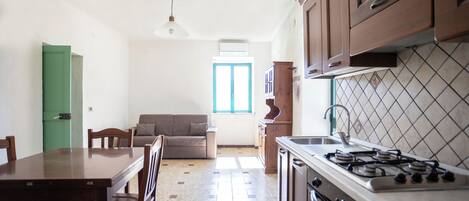 A compact kitchen with a dining table, chairs, a sofa, and a window providing natural light.