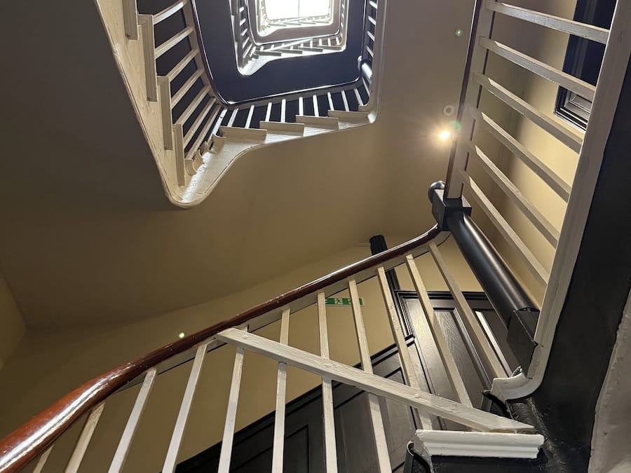 A staircase with a handrail, a black floor, and a light fixture above.