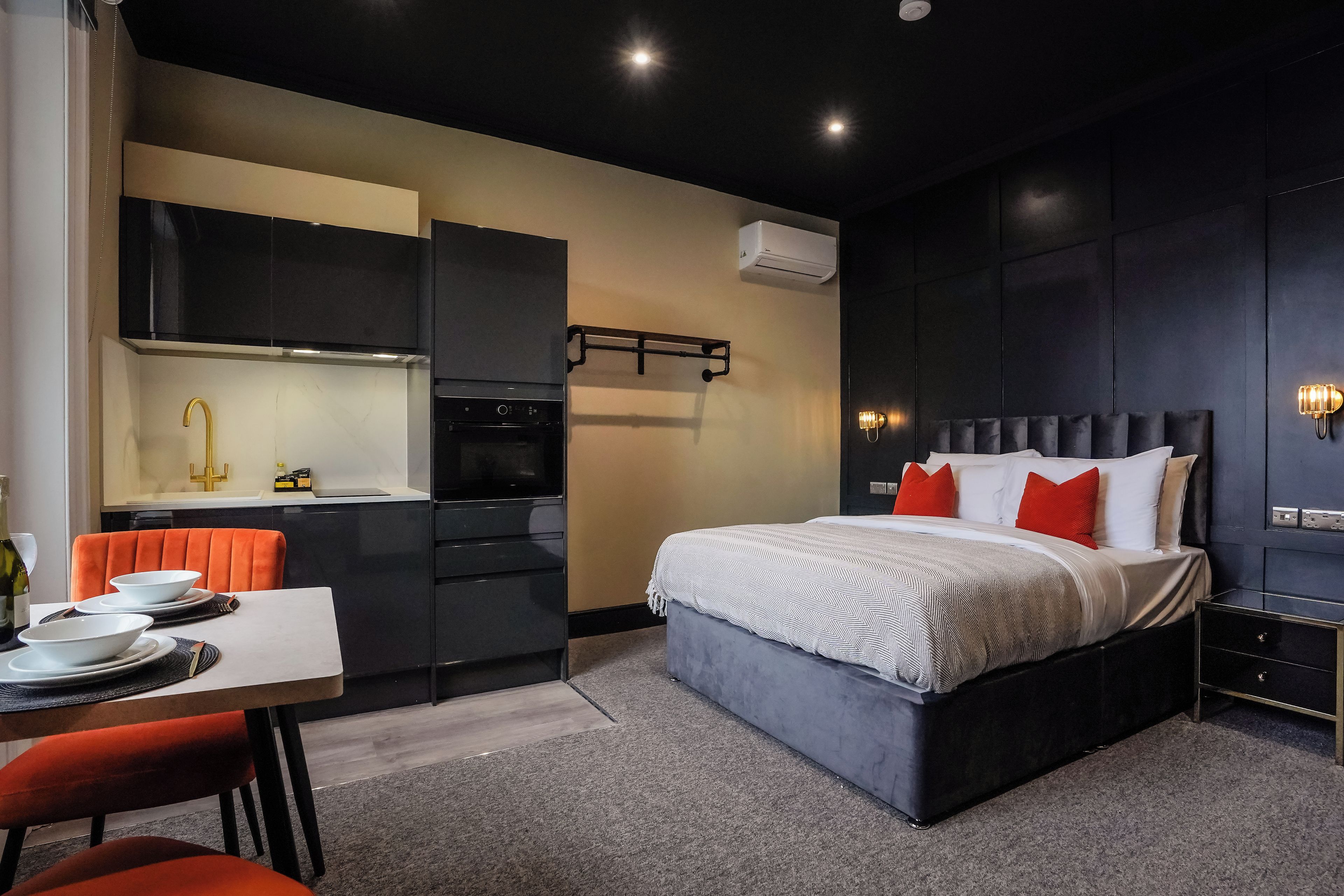 Habitació d'hotel moderna amb un llit, taules de nit, un escriptori amb cadires, zona de cuina i aire condicionat.