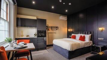 Quarto de hotel moderno com cama, escrivaninha e cozinha compacta.