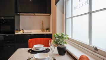 A modern kitchen with dark cabinets, a red chair, and a dining table set with white plates and a potted plant.