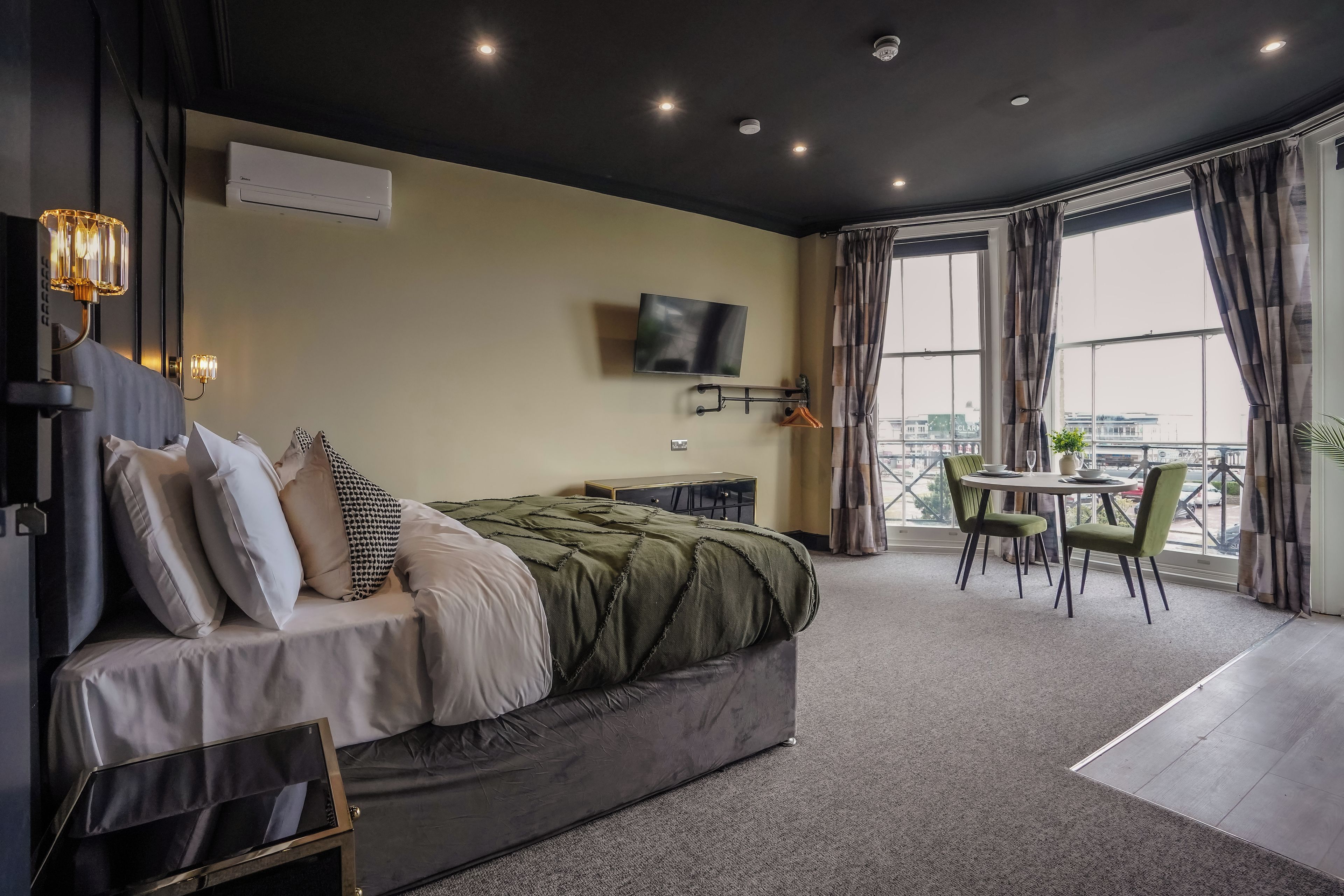 A modern bedroom with a bed, bedside table, TV, and a balcony with a table and chairs.