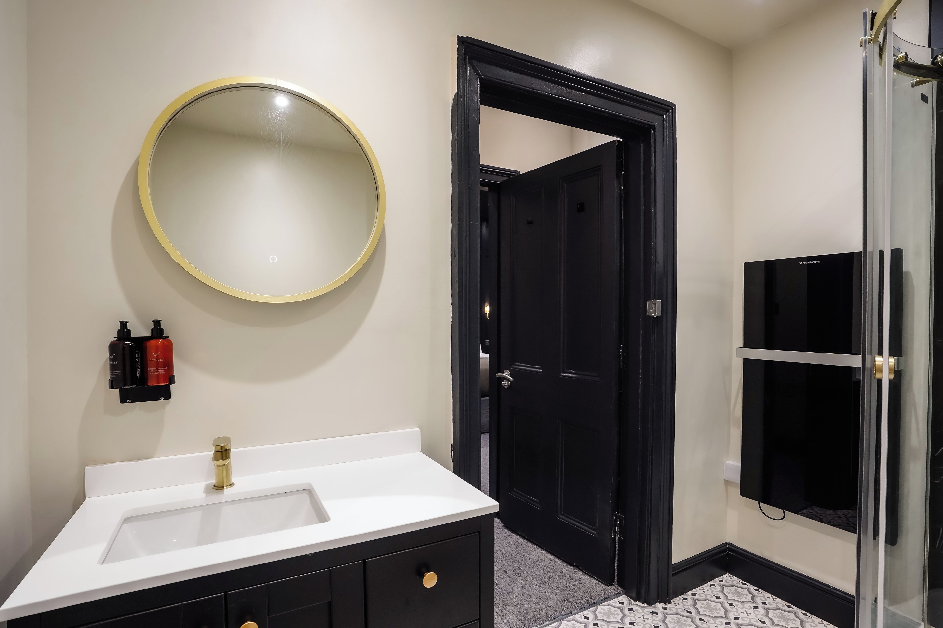 Une salle de bain avec un lavabo blanc, un miroir rond et une porte noire.
