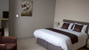 Un dormitorio con cama, una silla y un cuadro en la pared.