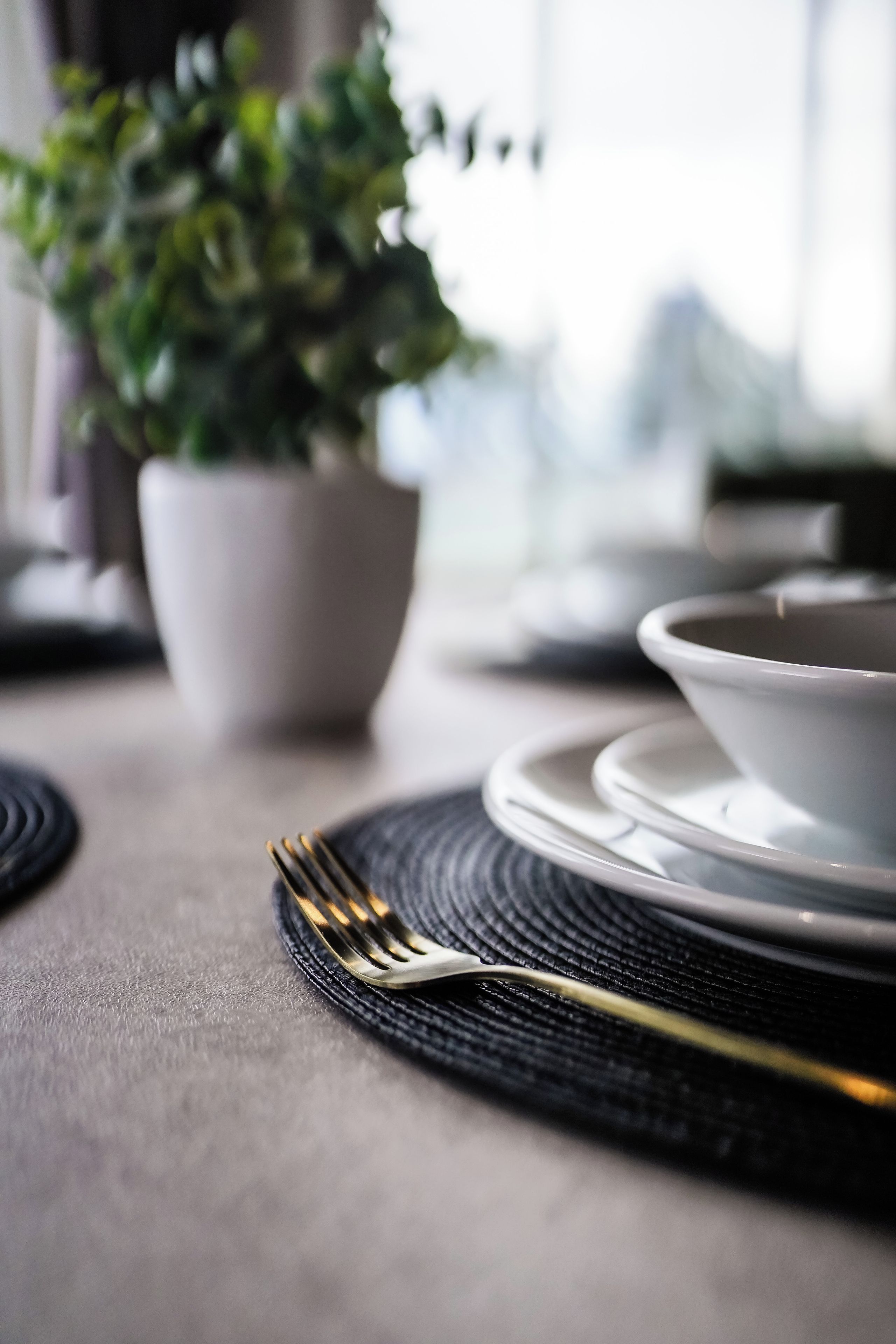 Een tafel gedekt met een witte kom, een gouden vork en een zwarte placemat.